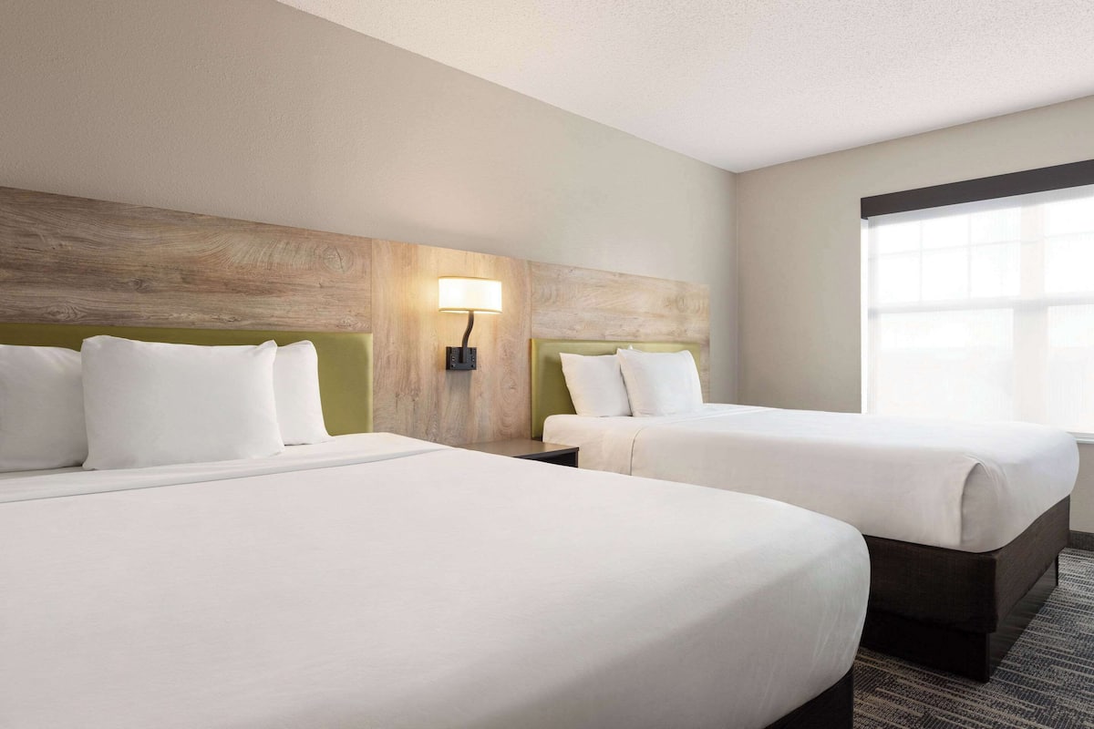A hotel room with two beds, a nightstand with a lamp, and a large window.