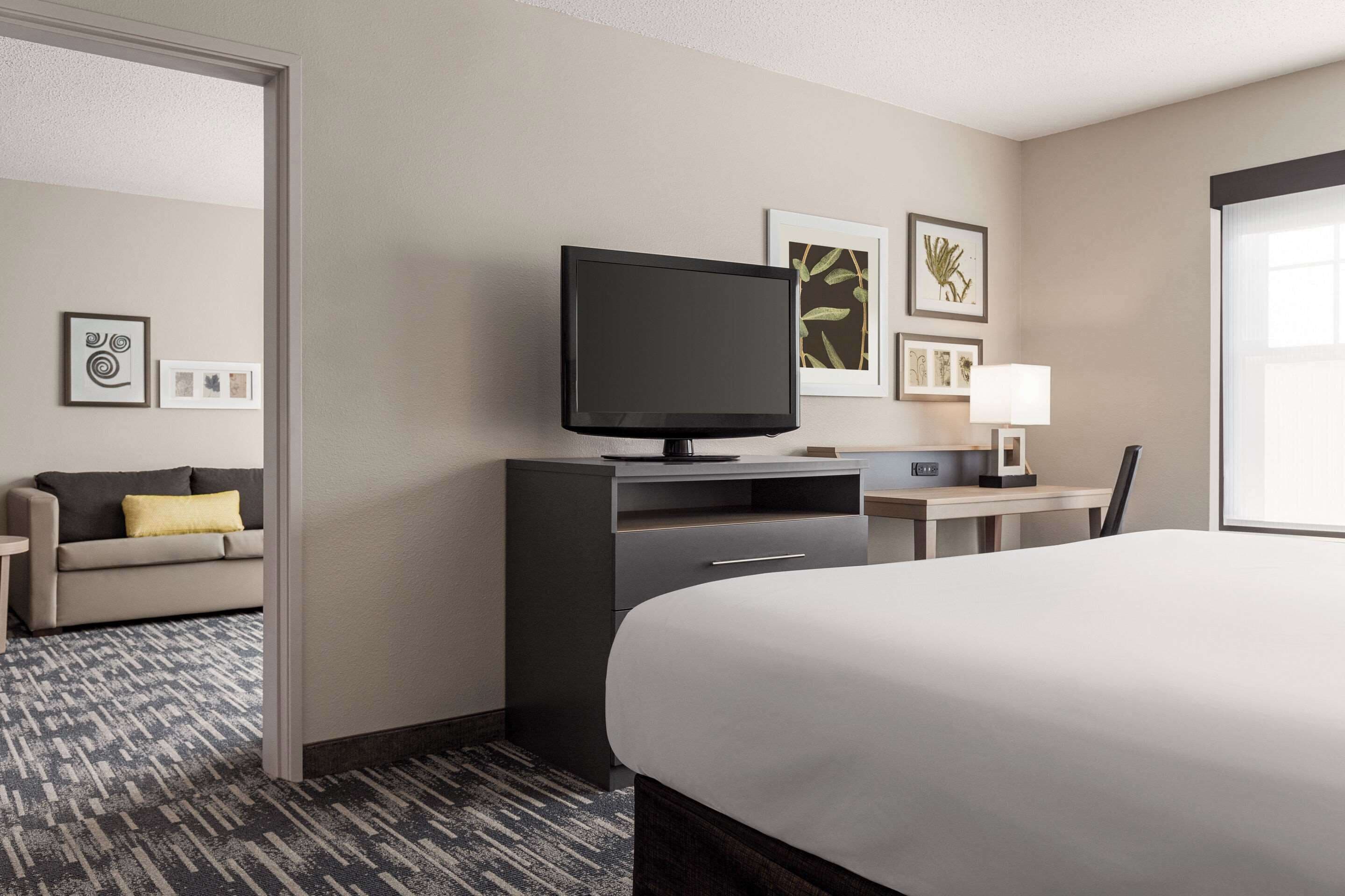 Quarto de hotel com cama, escrivaninha com computador, televisão e sofá.