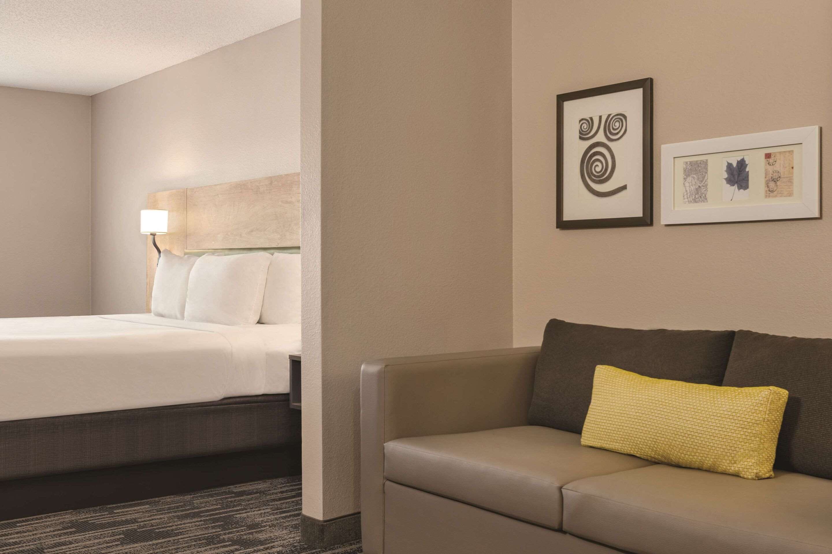 A hotel room with a bed, a sofa, and two framed artworks on the wall.