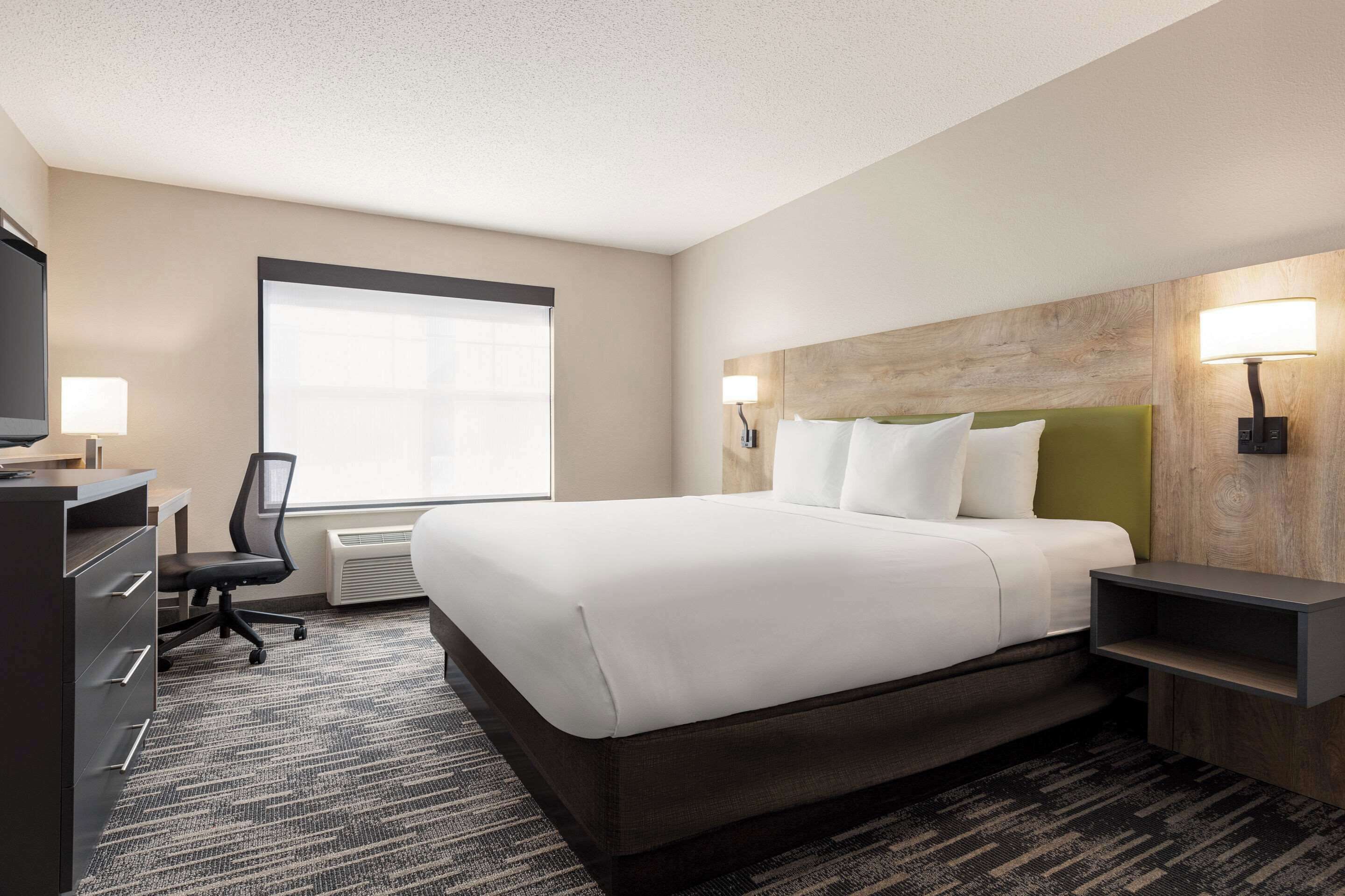 A hotel room with a large bed, a desk with a chair, a television, and two wall-mounted lamps.