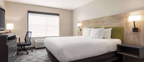 A hotel room with a large bed, a desk with a chair, a television, and two wall-mounted lamps.