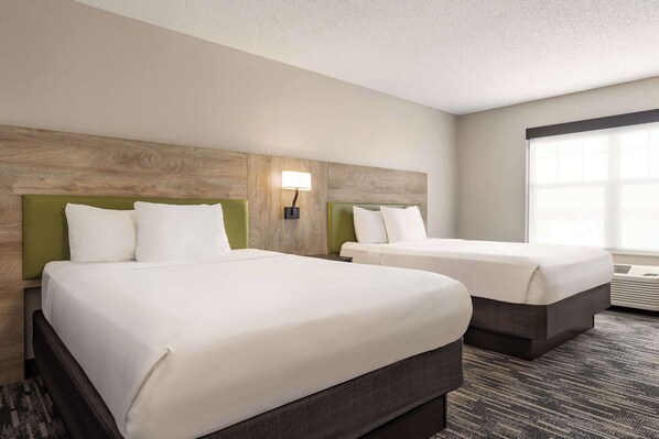 A hotel room with two beds, a wooden headboard, a green accent wall, and a large window.