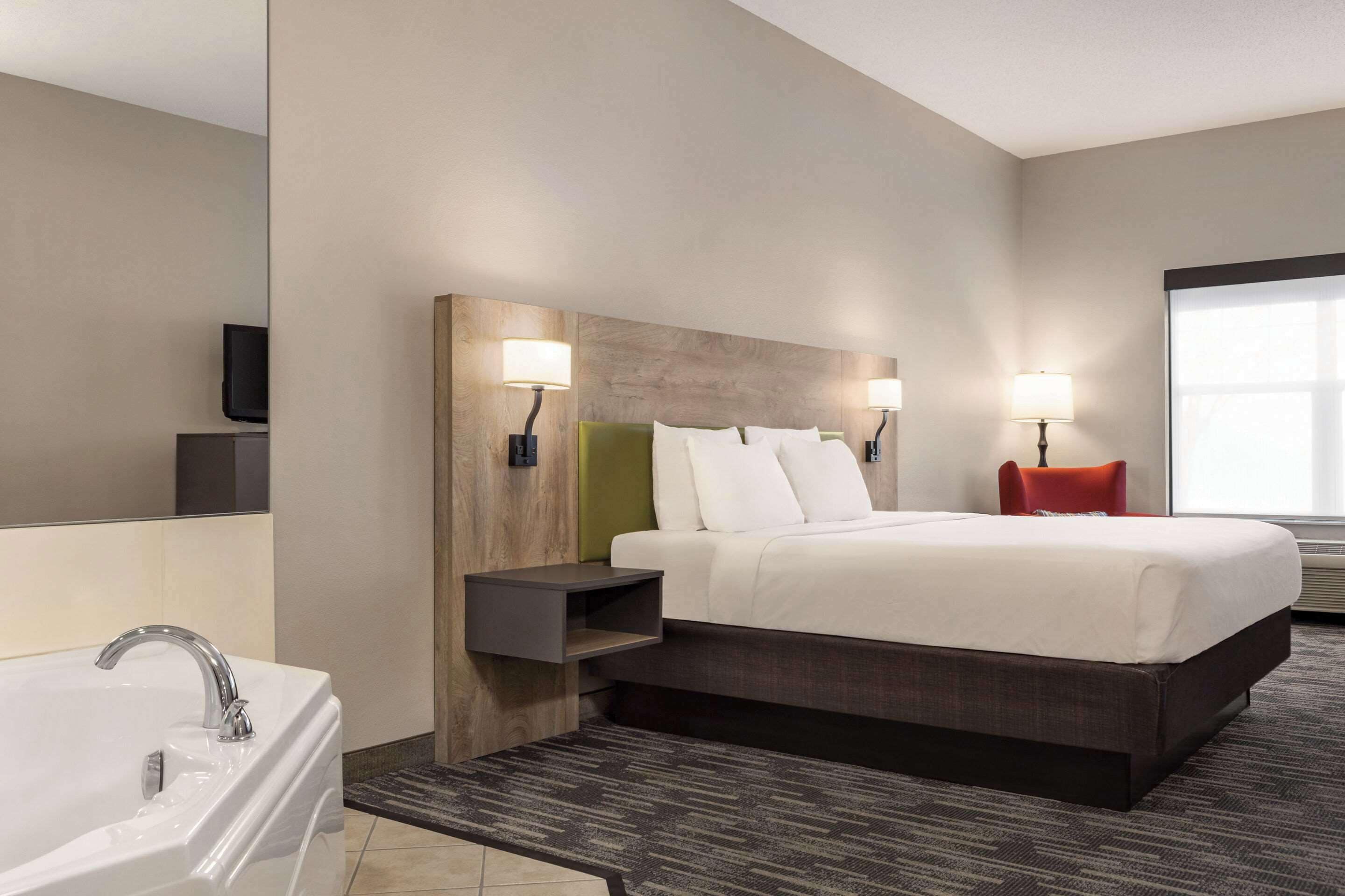 A modern hotel room with a large bed, a built-in nightstand, a wall-mounted TV, and a window with natural light.