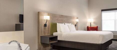 A modern hotel room with a large bed, a built-in nightstand, a wall-mounted TV, and a window with natural light.