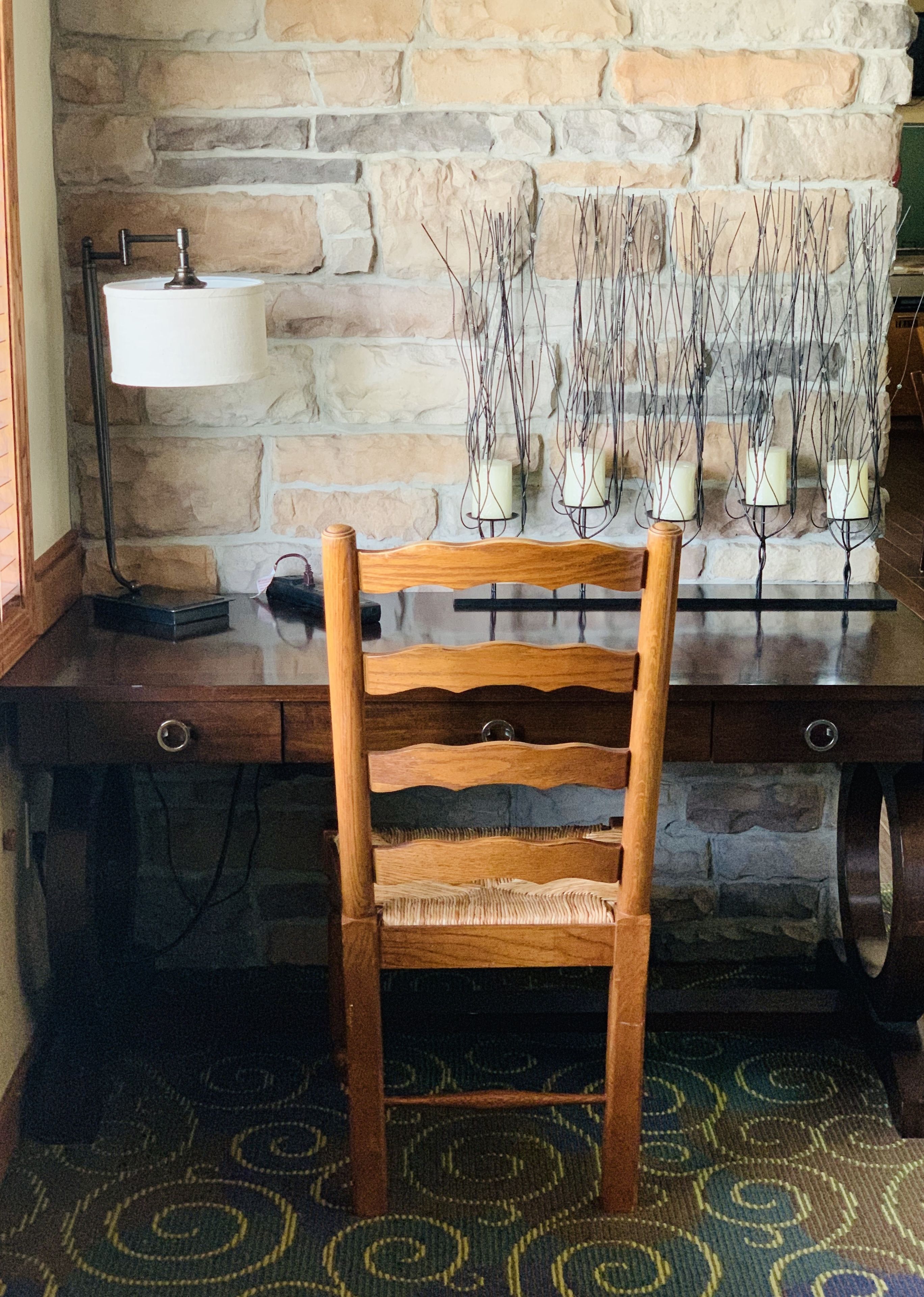 Une chaise en bois devant un mur de pierre, avec des bougies et une lampe.