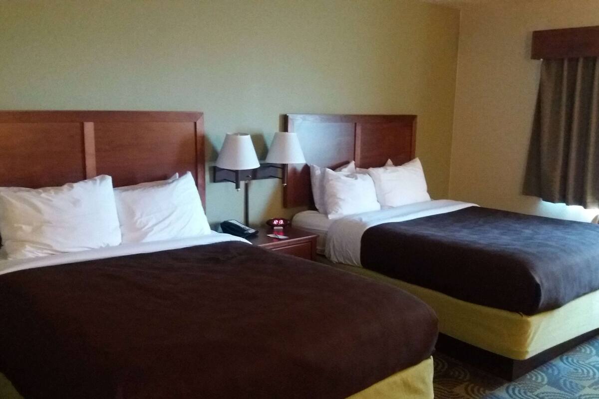 A hotel room with two beds, each with a wooden headboard, white bedding, and a nightstand with a lamp and a clock.