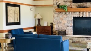 A living room with a blue sofa, a fireplace, a television, and a wooden balcony. - AmericInn by Wyndham Kewanee (Kewanee)