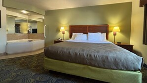 A hotel room with a large bed, two bedside lamps, a nightstand, a mirror, and a bathroom with a bathtub and toilet. - AmericInn by Wyndham Kewanee (Kewanee)