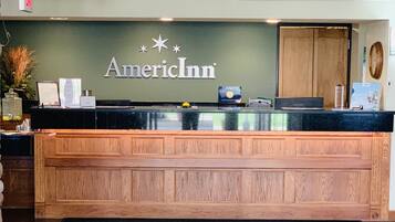 A reception desk with a wooden finish, a green wall with the 'American Inn' logo, and a black doormat with the same logo.