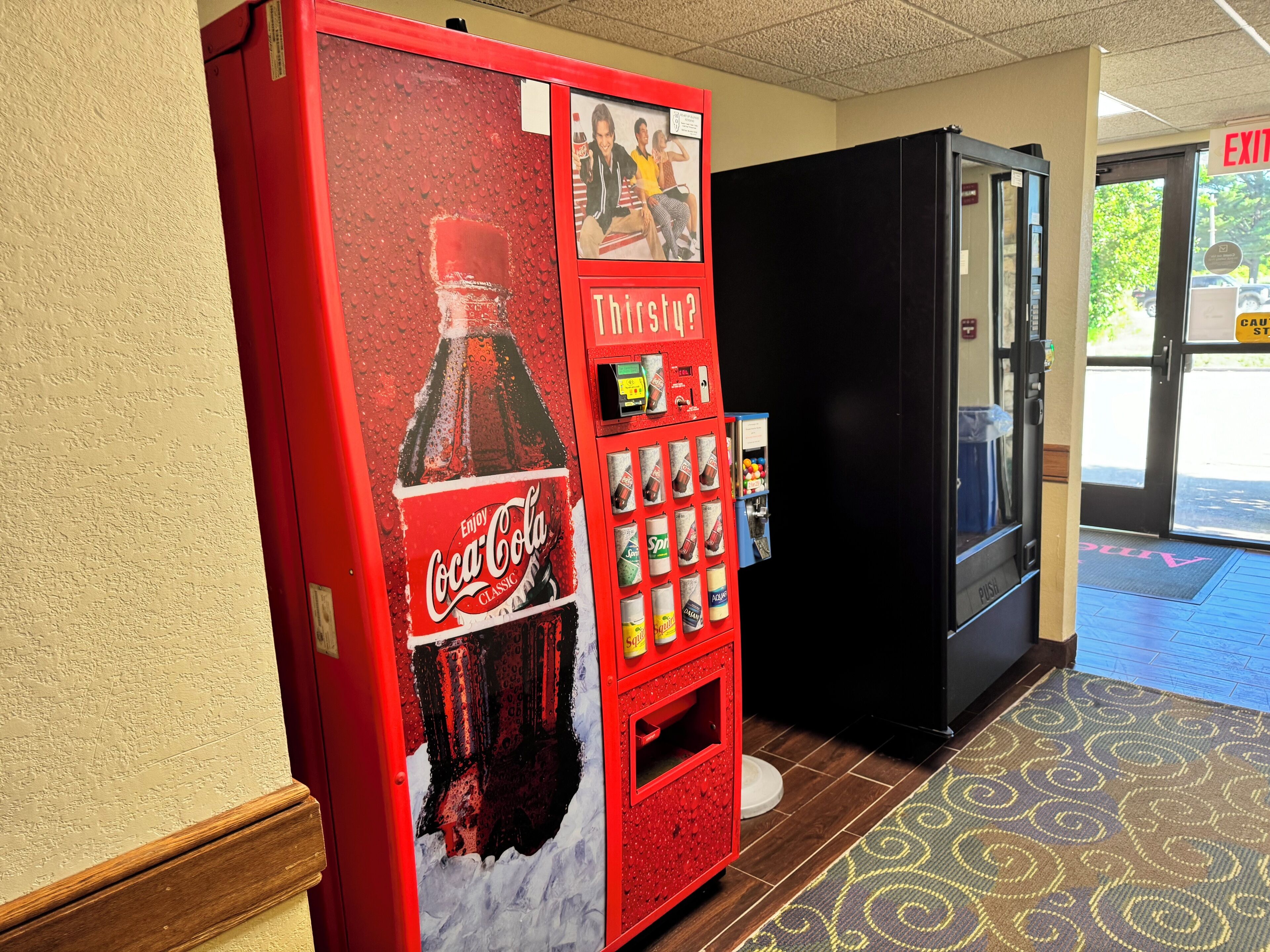 A Coca-Cola vending machine and a black refrigerator in a hotel lobby.