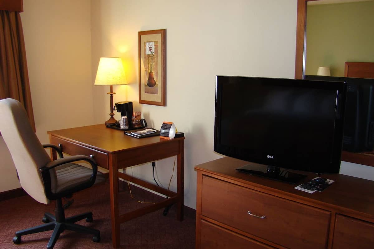 A hotel room with a desk, chair, television, lamp, and a framed picture on the wall.