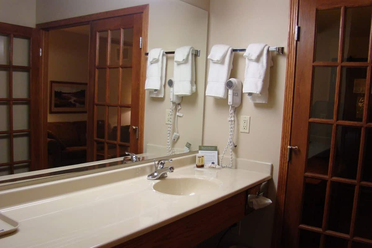A bathroom with a long sink, a mirror, a hairdryer, and a towel rack.