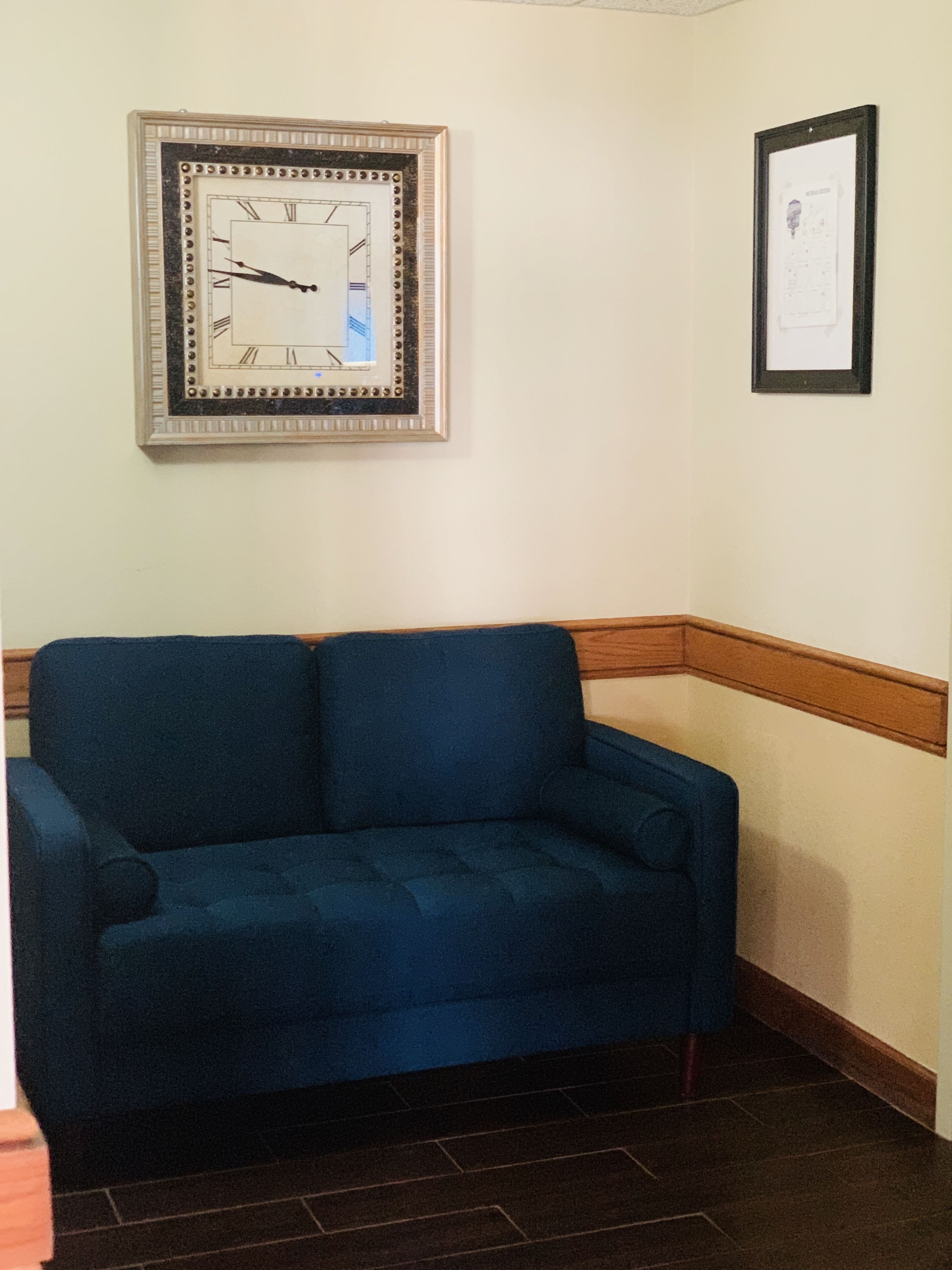 A blue sofa in a corner with a framed clock and a certificate on the wall.