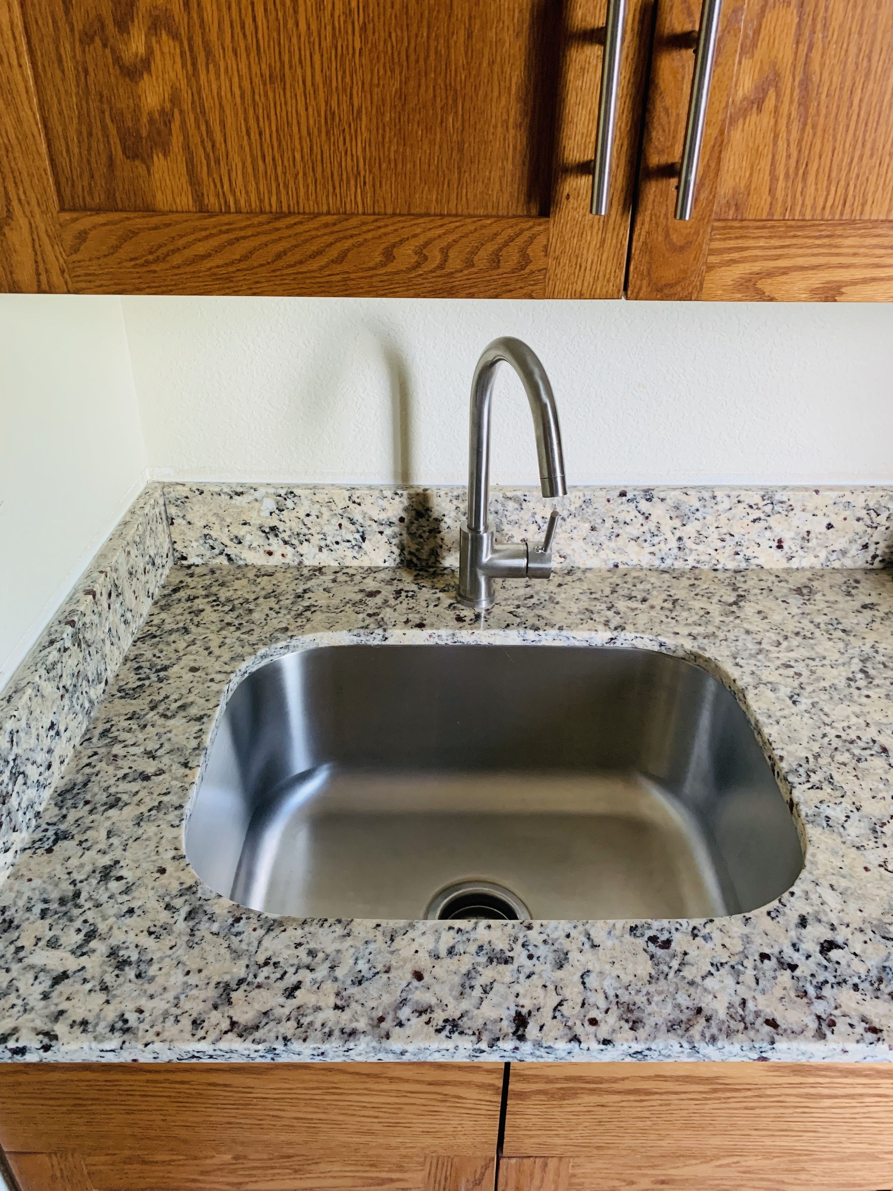 A kitchen with a stainless steel sink, granite countertop, wooden cabinets, and a stainless steel faucet.