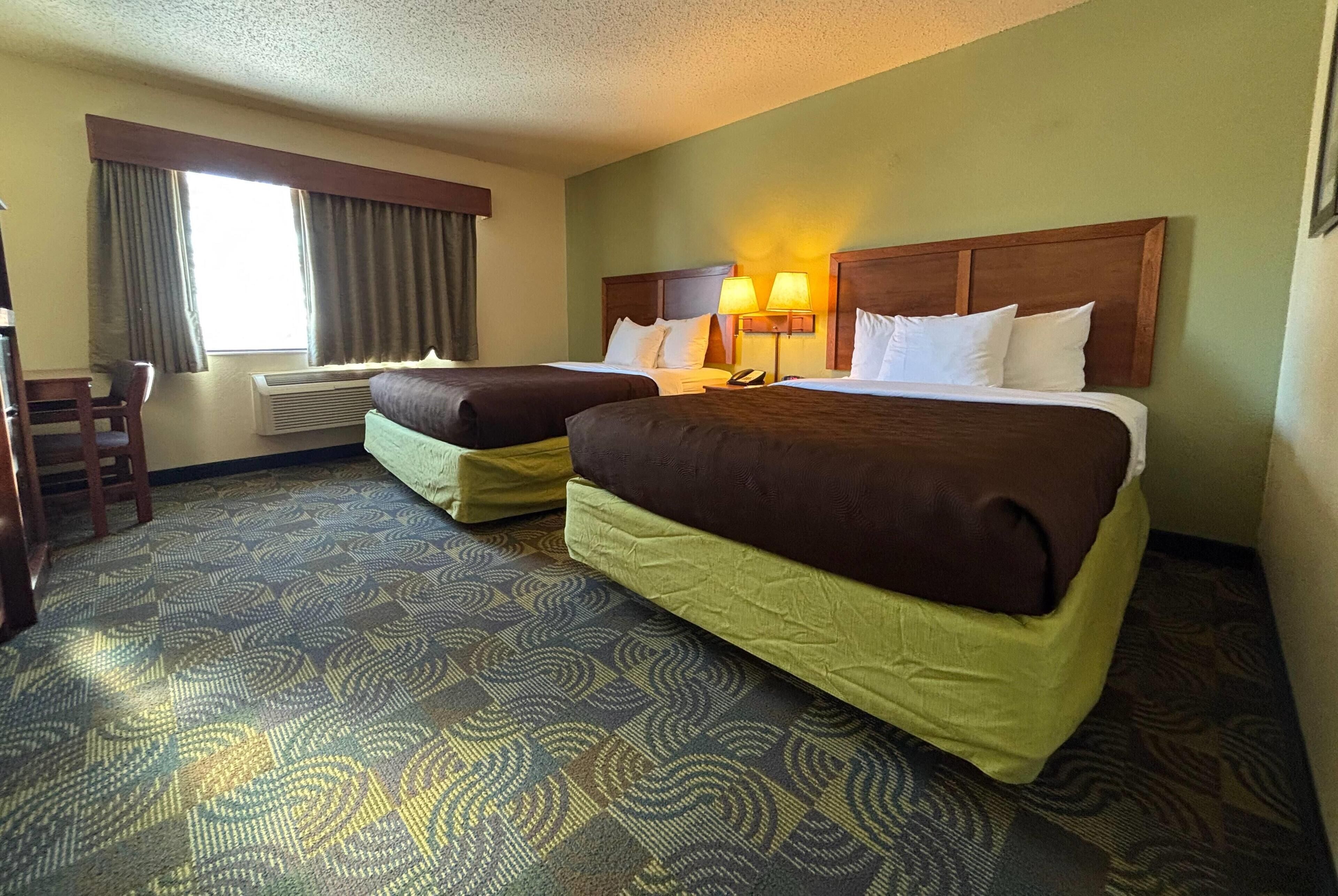 A hotel room with two beds, a desk, and a chair.