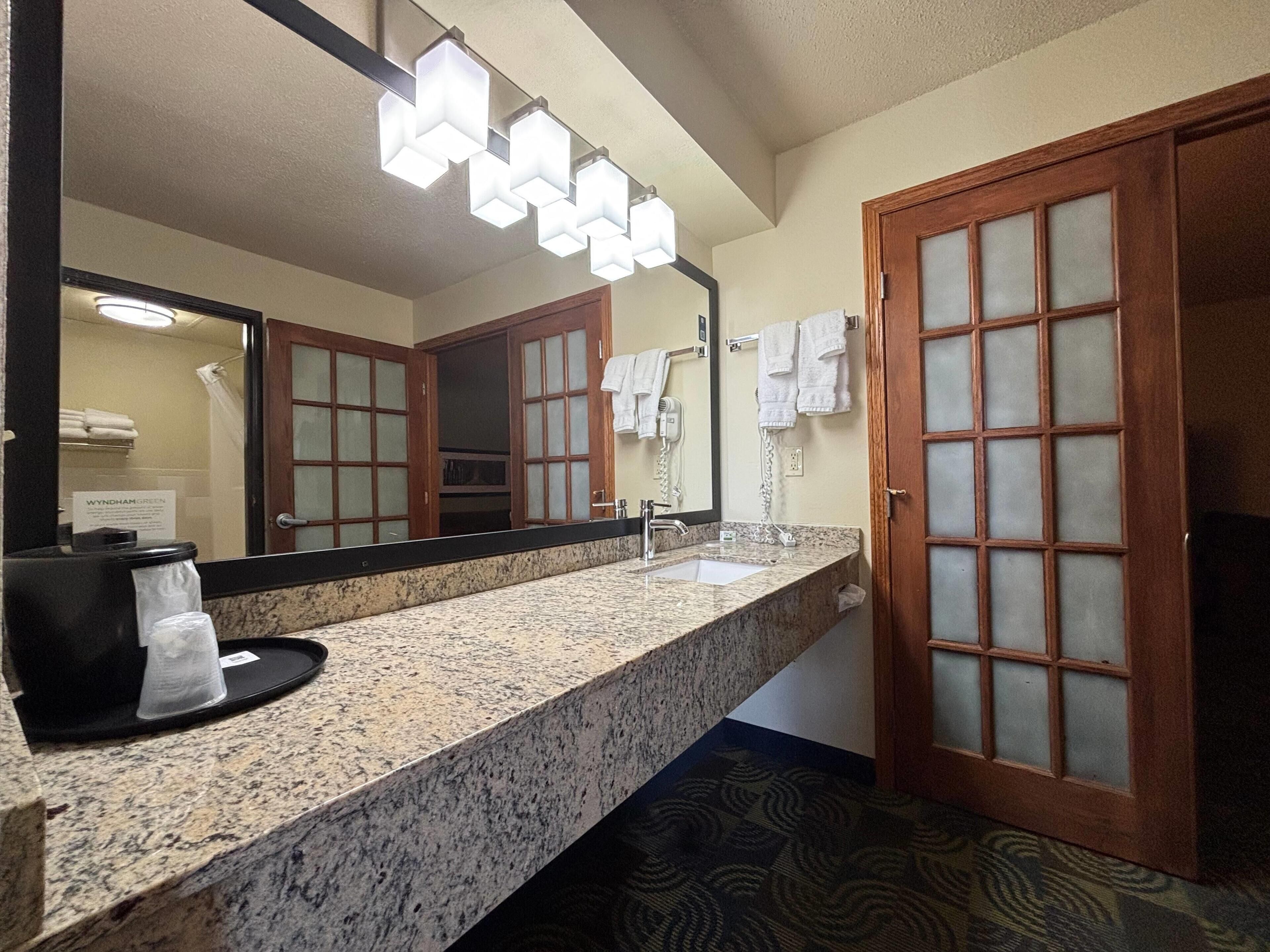 A bathroom with a granite countertop, a sink, a mirror, and a towel rack.