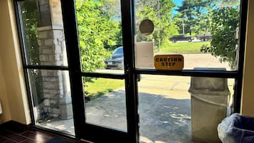A hotel entrance with a caution step sign, a doormat, and a view of the parking area.