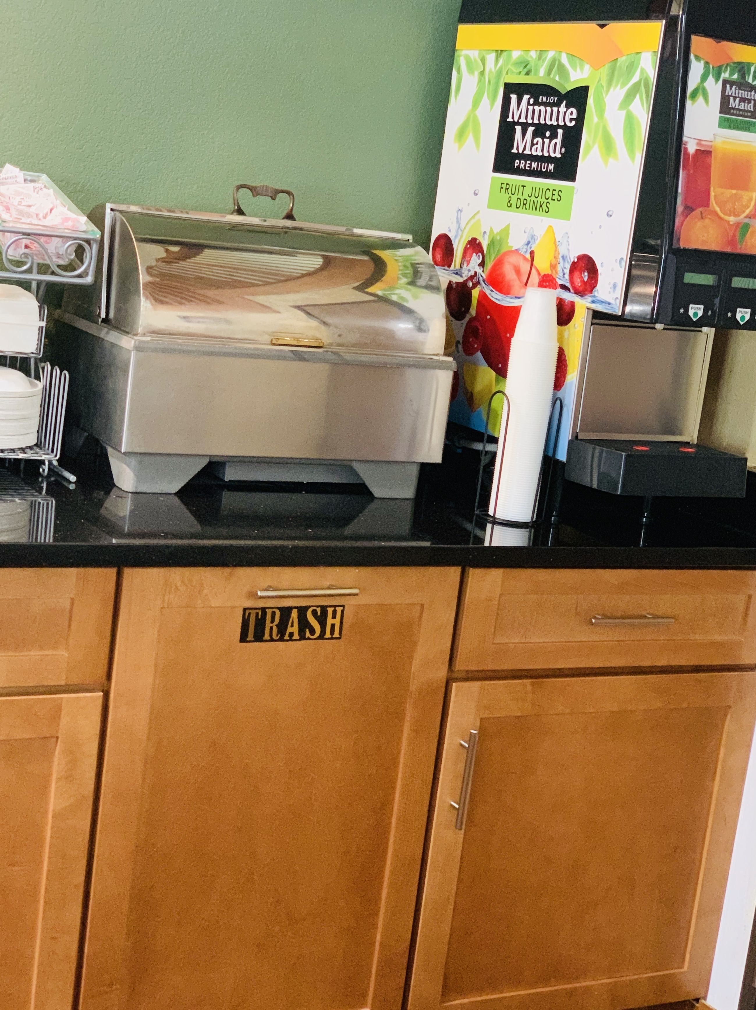 Disposição de buffet com uma lixeira identificada com a etiqueta 'TRASH' e um refrigerador de suco Minute Maid.