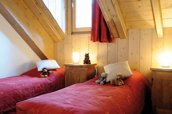 A cozy room with two beds, each with a red bedspread and pillows, wooden headboards, and a window with a red curtain. - Résidence Lagrange Vacances Les Arolles (Saint-Gervais-les-Bains)