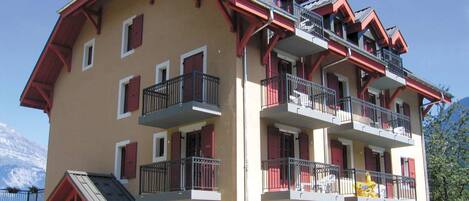 Un hotel de varios pisos con balcones, contraventanas rojas y montañas al fondo.