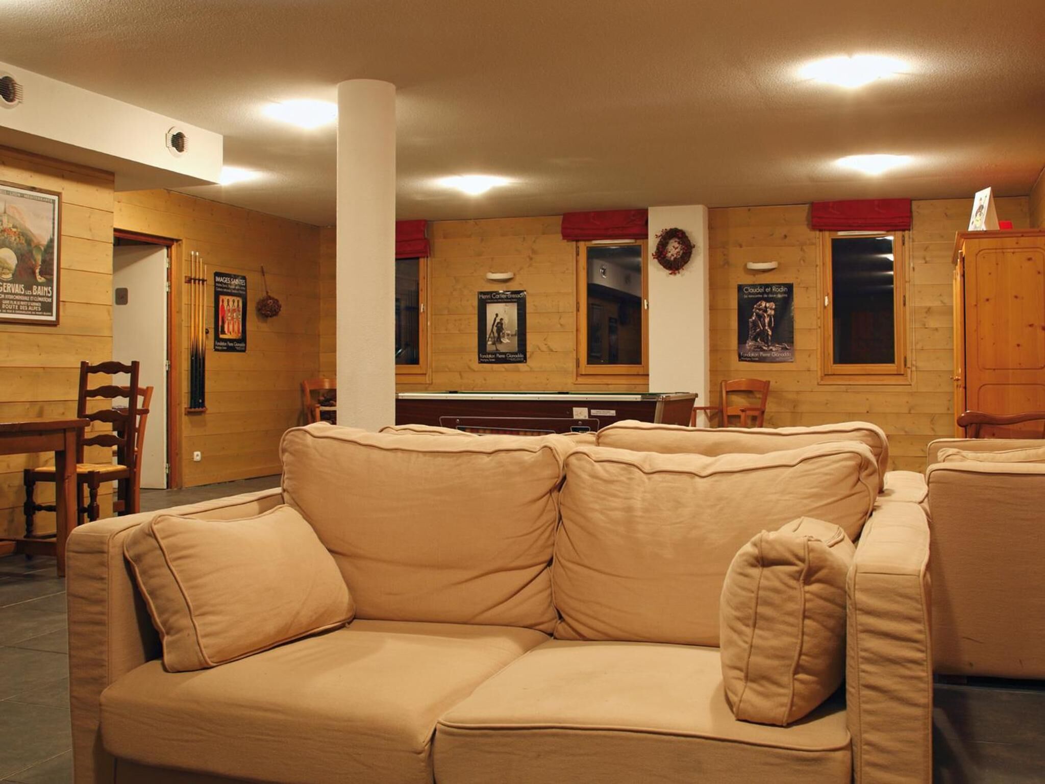 A cozy room with a beige sofa, wooden walls, and a billiards table.