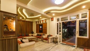 A spacious living area with a sofa set, a coffee table, and a TV. There is a wooden cabinet and a door leading outside. - Hotel Encounter Nepal (Kathmandu)