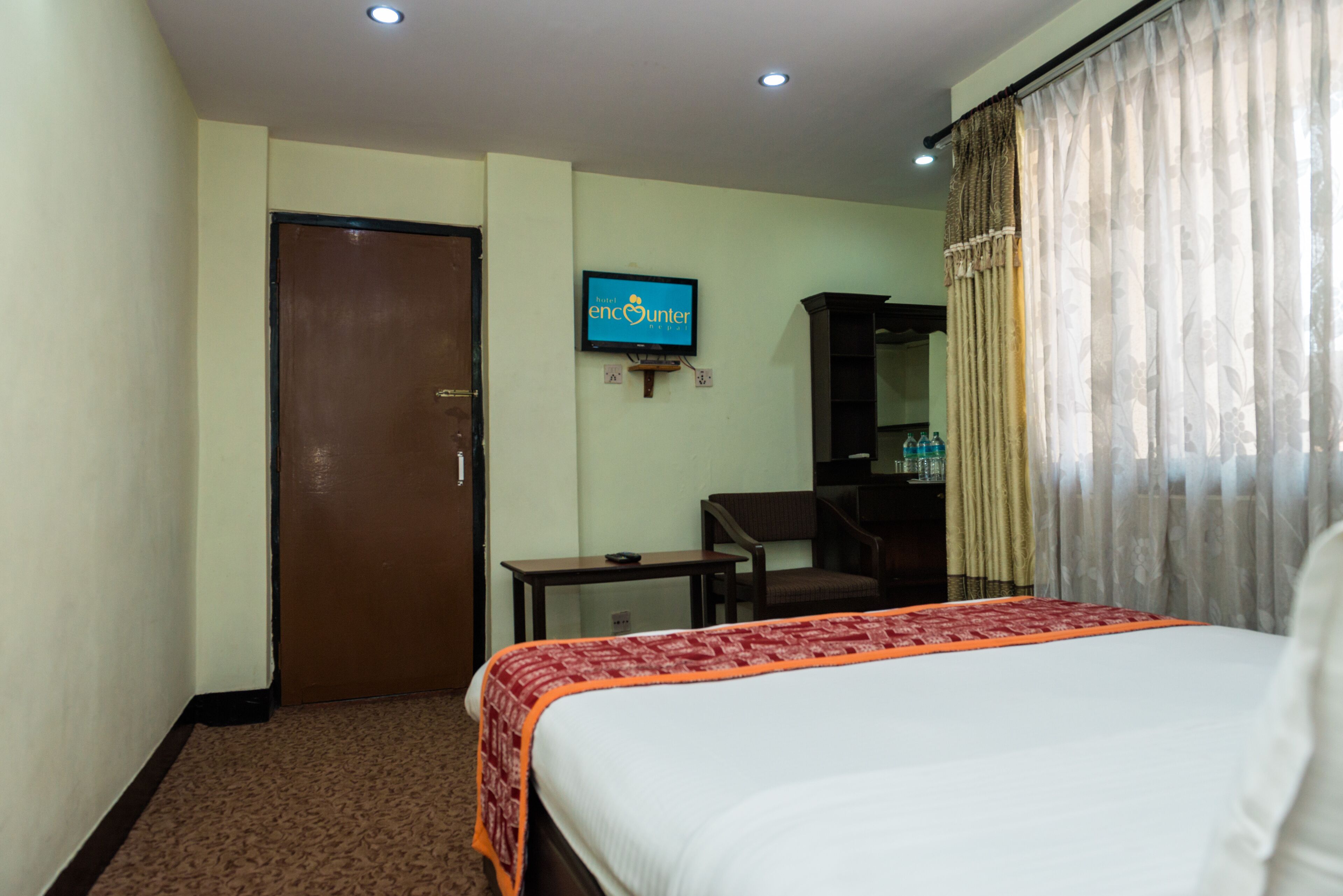 Ein Hotelzimmer mit einem Bett, einem an der Wand befestigten Fernseher, einem Schreibtisch und einer Tür.