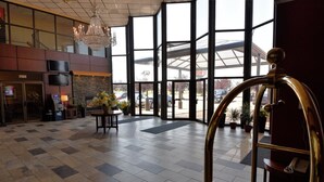 Un hall d’entrée spacieux, agrémenté d’un lustre, d’une cheminée en pierre et d’une grande porte vitrée donnant sur l’extérieur.