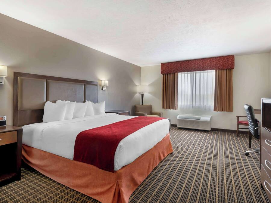 A hotel room with a large bed, a desk, a chair, a TV, and a window with curtains.