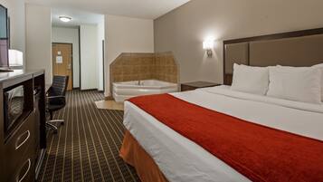 Quarto de hotel com cama, secretária, cadeira, banheiro com banheira e mesa de cabeceira.