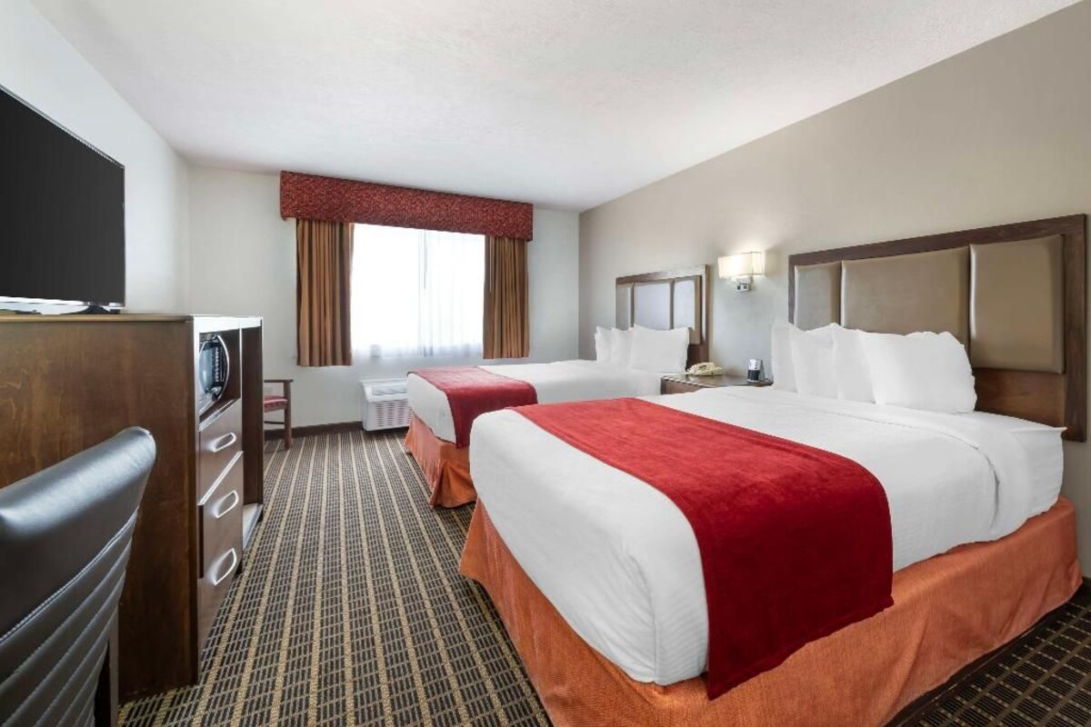 A hotel room with two beds, a desk, a television, and a window with curtains.