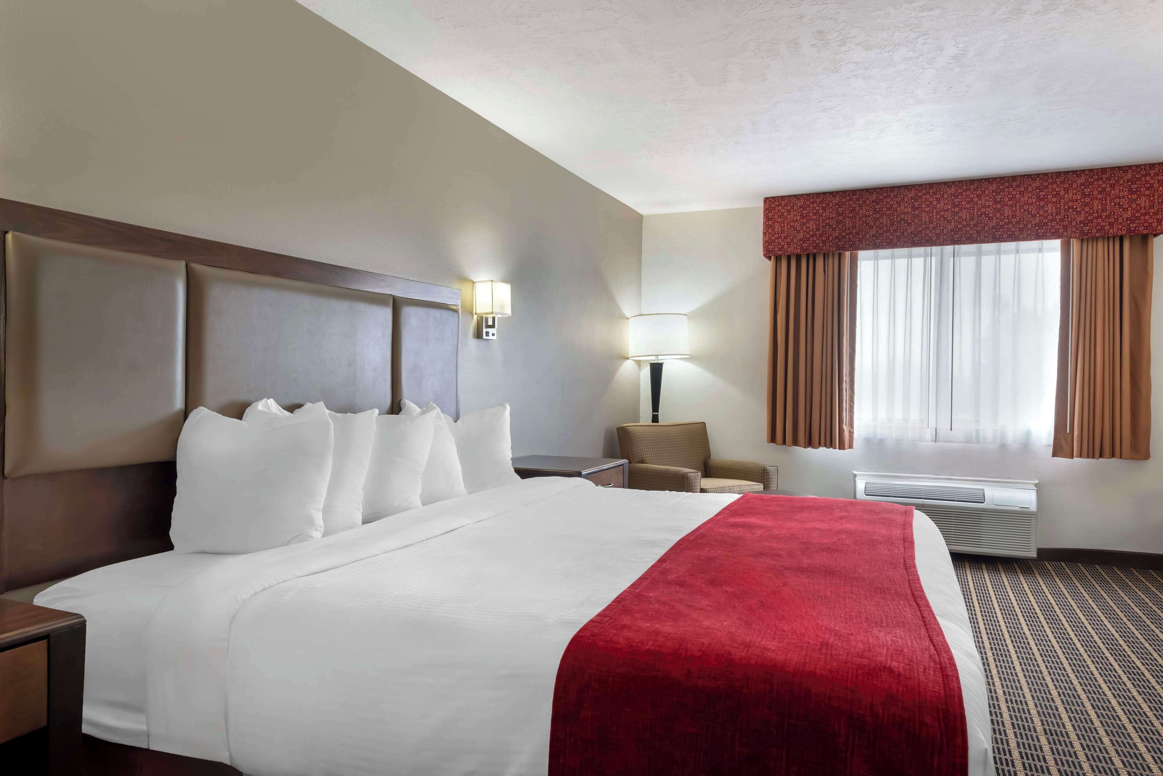 Une chambre d’hôtel avec un grand lit, une table de chevet, une chaise, une lampe et une fenêtre avec des rideaux.
