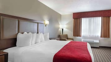 Une chambre d’hôtel avec un grand lit, une table de chevet, une chaise, une lampe et une fenêtre avec des rideaux.