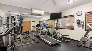 A gym with various exercise equipment, a ceiling fan, and a clock on the wall.