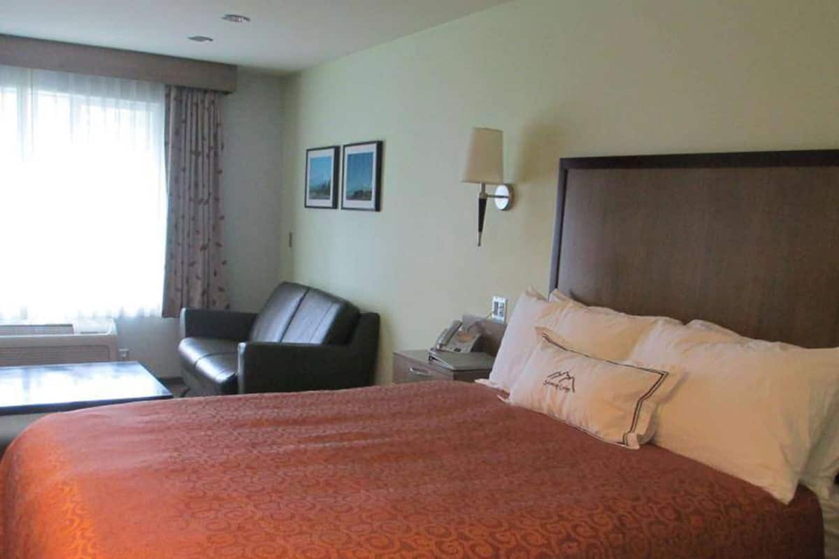 A hotel room with a large bed, a desk with a lamp, a chair, and two framed pictures on the wall.