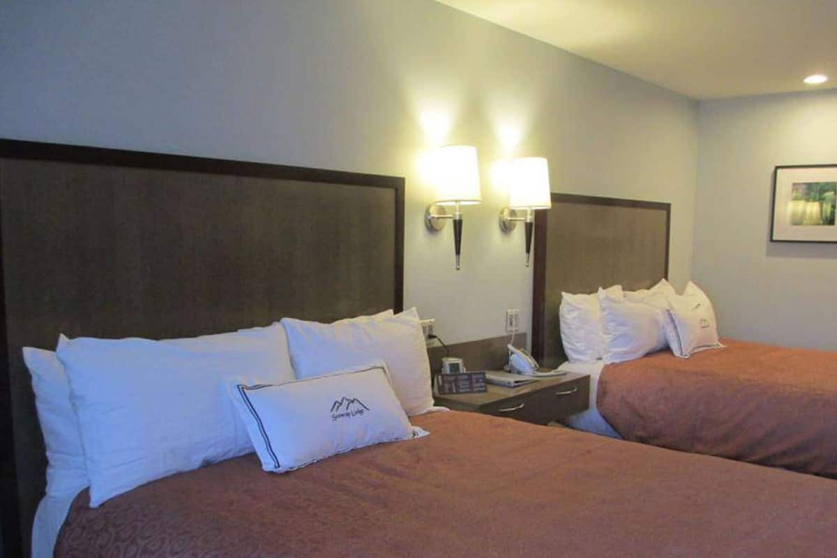 A hotel room with two beds, a bedside table with a lamp, a mirror, and a framed picture on the wall.