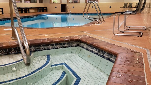 A swimming pool area with a tiled hot tub, a metal ladder, and lounge chairs.
