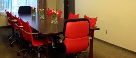 A conference room with a long table, red chairs, and vases with flowers.
