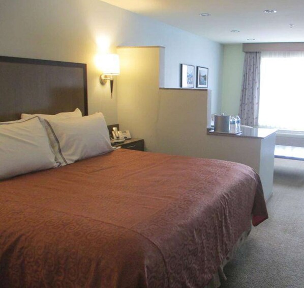 A hotel room with a large bed, a bedside table with a lamp, a small desk with a telephone, and a window with curtains. - Best Western Snowcap Lodge (Cle Elum)