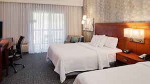 Une chambre d’hôtel avec deux lits, un bureau avec une chaise, une lampe et un téléphone.