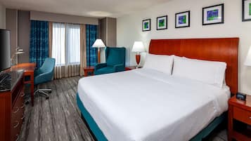 Una habitación de hotel con una cama grande, un escritorio con computadora, una silla, dos lámparas y un televisor.