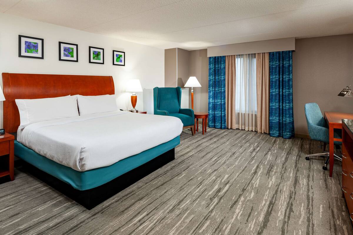 Une chambre d’hôtel avec un grand lit, un bureau, une chaise, une télévision et des tableaux encadrés au mur.