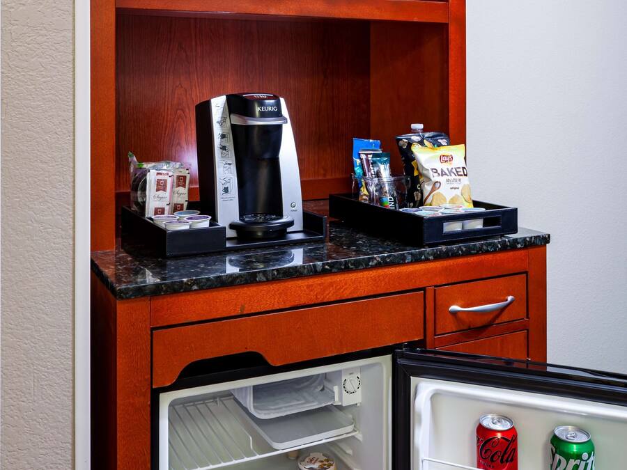 A compact kitchenette with a microwave, coffee maker, and a mini-fridge containing beverages and snacks.