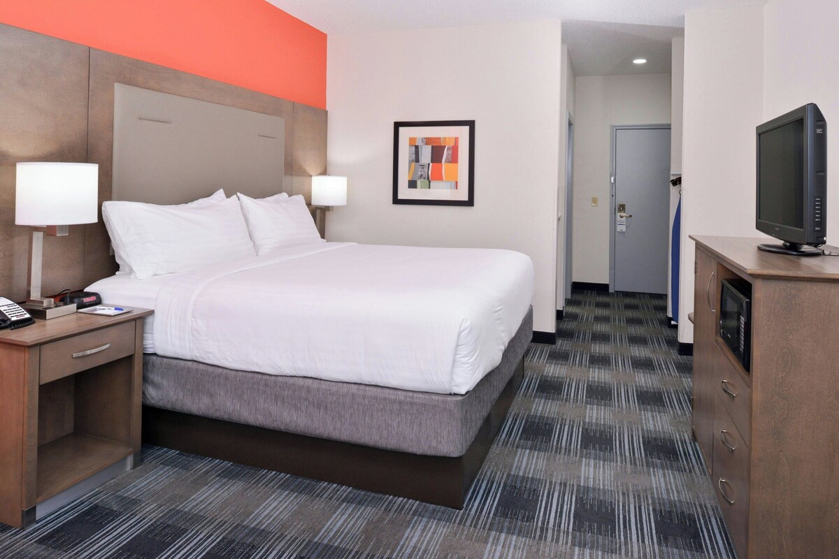 A hotel room with a bed, bedside lamps, a desk with a telephone, a television, and a framed picture on the wall.
