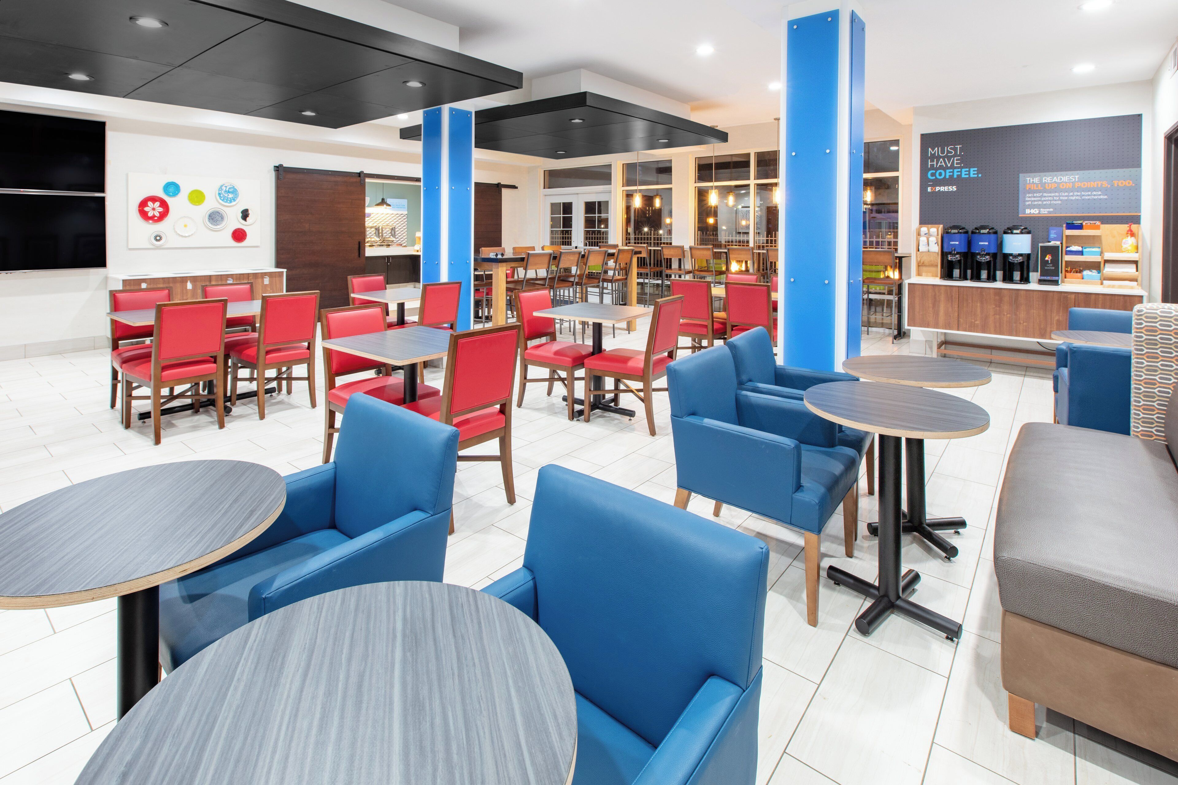 A modern cafe interior with red and blue seating, a coffee bar, and a wall with a coffee-themed sign.