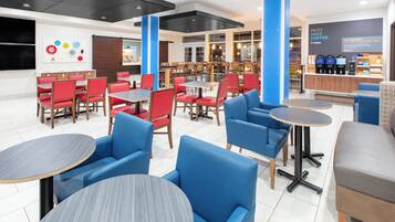 A modern cafe interior with red and blue seating, a coffee bar, and a wall with a coffee-themed sign.