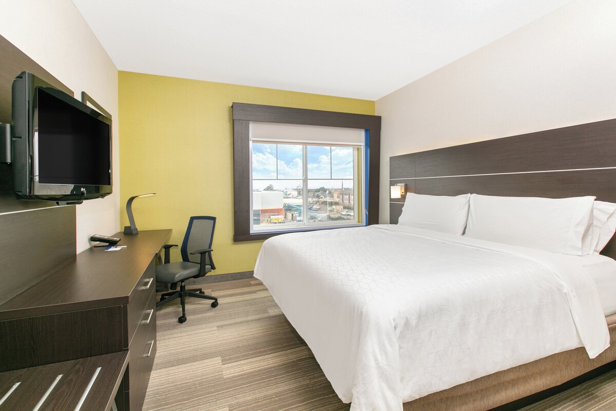A hotel room with a bed, a desk, a chair, a television, and a window with a city view.