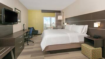 A hotel room with a bed, desk, chair, television, and a view of the outdoors.