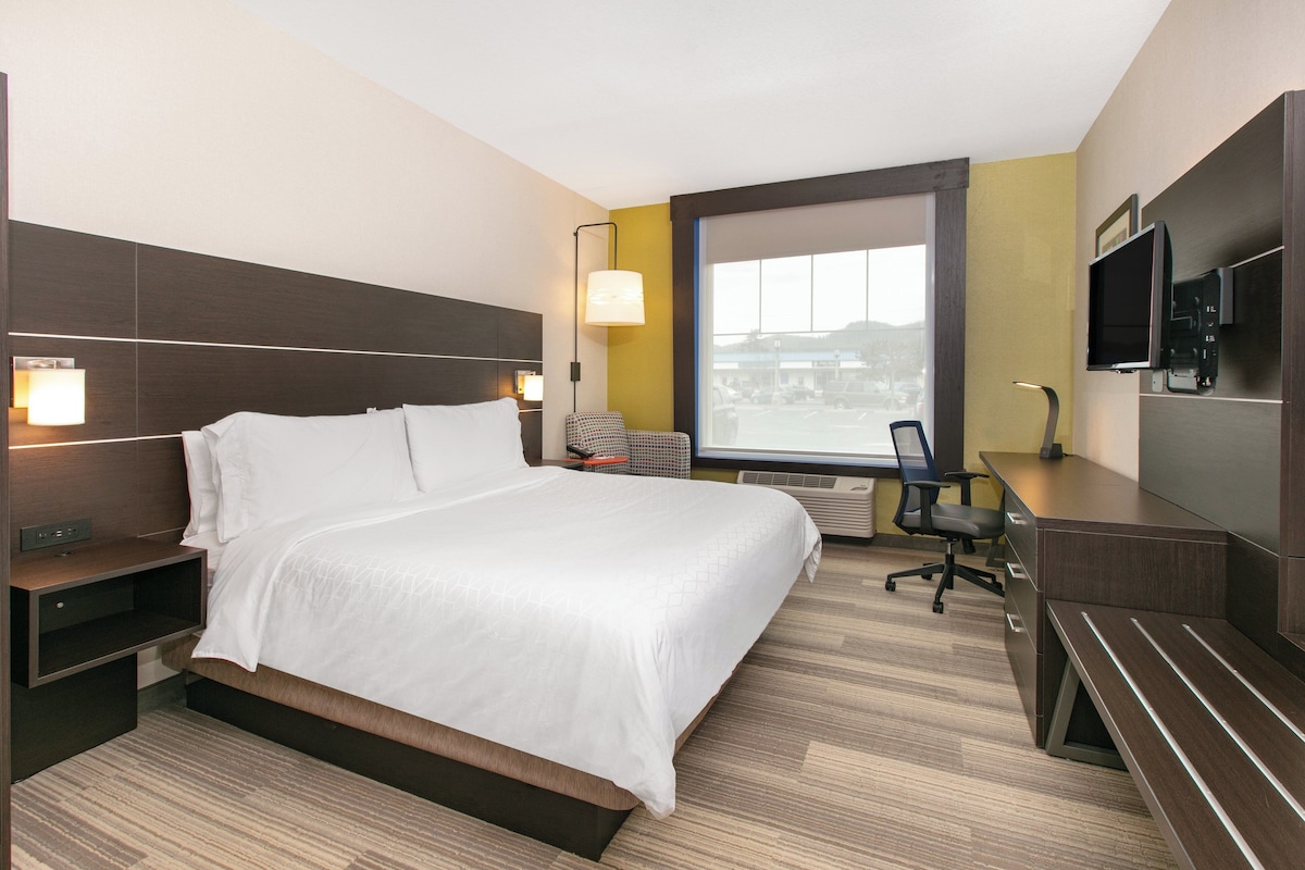 Une chambre d’hôtel équipée d’un lit, d’un bureau, d’une chaise, d’une télévision et d’une fenêtre donnant sur la ville.