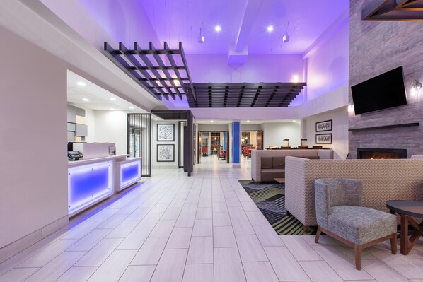 A hotel lobby with a reception desk, seating area, and a TV mounted on the wall. - Holiday Inn Express Hotel & Suites Seaside-Convention Center by IHG (Seaside)